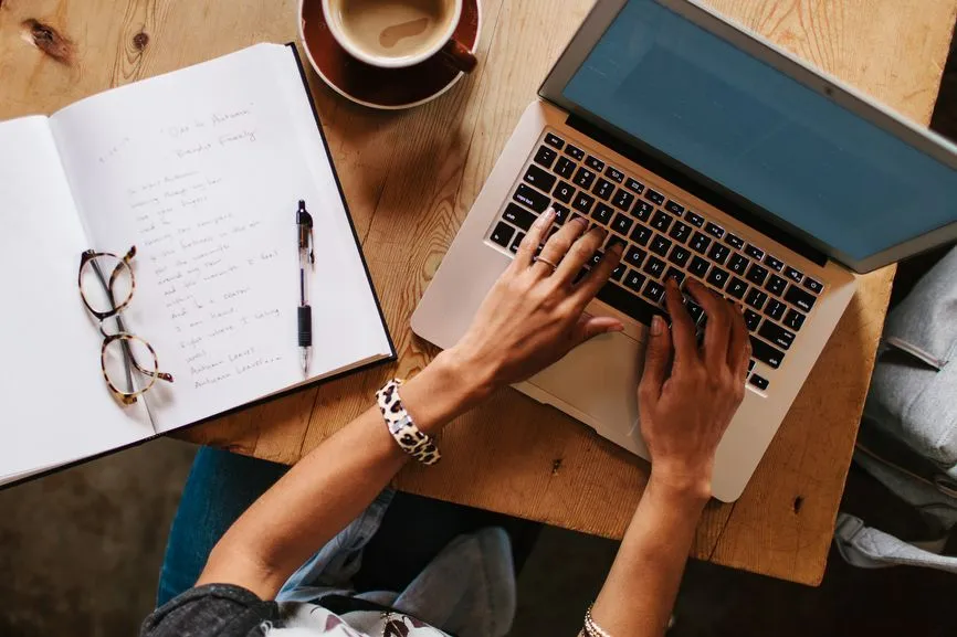 A notebook, coffee, and open laptop on a wooden desk, representing a calm, focused browsing session